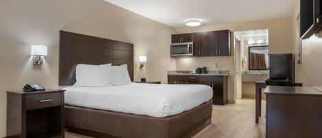 Habitación de hotel con cama, mesita de noche, lámpara y una zona de kitchenette con microondas y refrigerador.