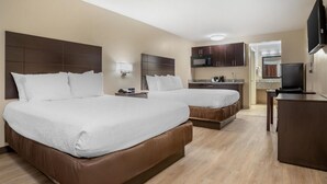 Ett hotellrum med två sängar, ett litet kök, en TV och ett badrum som syns genom en öppen dörr.