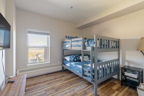 A bunk bed room with a window, a desk, and a lamp.