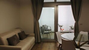 A living room with a sofa, a glass door leading to a balcony, and a dining area with chairs and a table. - Central Apartment Olbia-San Simplicio (Oblia)