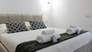 A neatly made bed with patterned pillows, a rolled towel, and a folded towel on a dark green bedspread. - Central Apartment Olbia-San Simplicio (Oblia)
