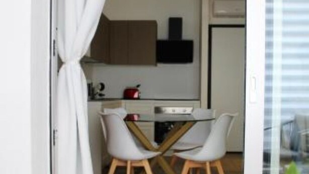 A modern kitchen with white cabinets, a black range hood, and a red pot on the countertop. There are two white chairs with wooden legs around a small table. - Central Apartment Olbia-San Simplicio (Oblia)