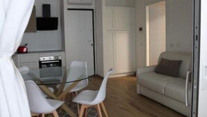 A compact living space with a kitchenette, a dining area with a glass table and chairs, and a sofa. - Central Apartment Olbia-San Simplicio (Oblia)