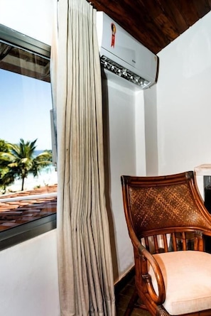 A room with a view of palm trees, a window with curtains, a wooden chair, and an air conditioning unit. - Pousada do Joab - Fernando de Noronha (Fernando de Noronha)