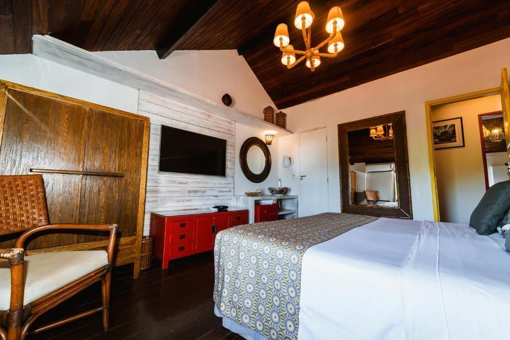 A bedroom with a bed, a chair, a dresser, a mirror, and a chandelier.