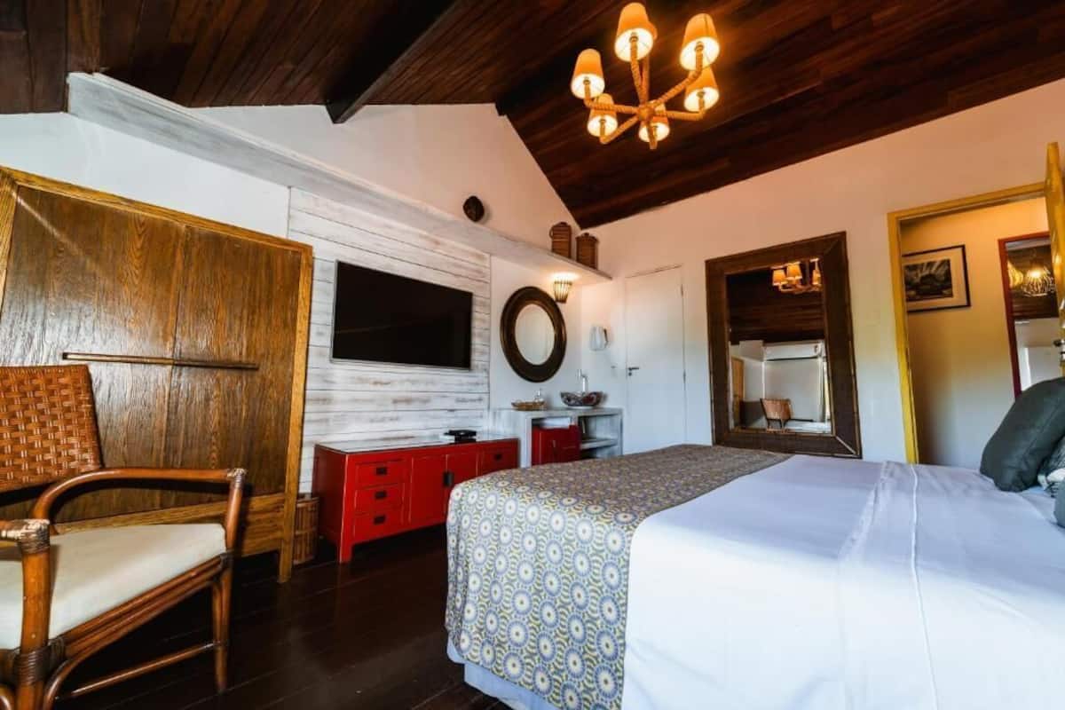 Quarto com cama, cadeira, cômoda, espelho e lustre.