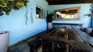 Una habitación con una gran mesa de madera, una planta en maceta, una planta colgante y un espejo en la pared.