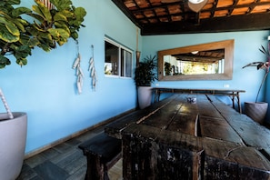 A room with a large wooden table, a potted plant, a hanging plant, and a mirror on the wall. - Pousada do Joab - Fernando de Noronha (Fernando de Noronha)
