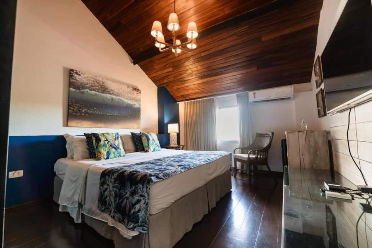 Quarto com cama, pintura, cadeira e mesa de vidro.