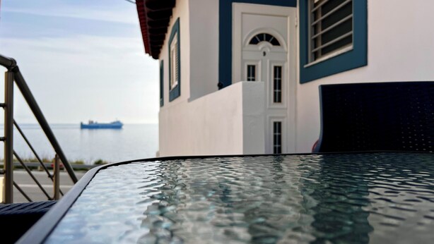 Ein Pool mit klarem Wasser, ein weißes Gebäude mit blauen Akzenten und ein Schiff in der Ferne auf dem Wasser.