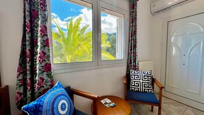 A room with two windows, a door, and a small table with a book. - Cozy studio near the beach (Avlakia)