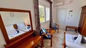 A hotel room with a bed, a desk, a chair, a small table, and a mirror. - Cozy studio near the beach (Avlakia)