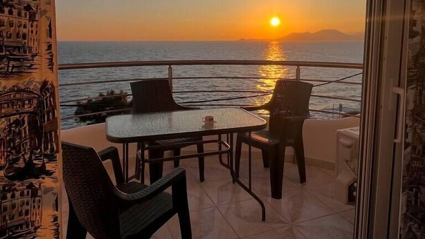 Een balkon met een tafel en stoelen, met uitzicht op een zonsondergang boven de zee.