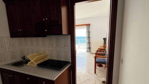 Een keuken met donkerhouten kasten, een spoelbak en een aanrecht. Er is uitzicht op een balkon met een stoel en een tafel, en de oceaan is in de verte te zien.