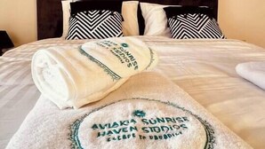 Een net opgemaakt bed met een witte en groene handdoek, een donker houten hoofdbord, en twee ingelijste objecten aan de muur.