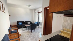 Een moderne woonkamer met een bank, stoelen, een salontafel en een keuken met een fornuis.