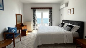 Een slaapkamer met een bed, een stoel, een bureau, een spiegel en uitzicht op zee.
