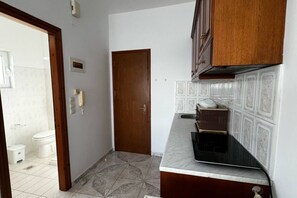 A narrow hallway with a wooden door, a kitchen area with a microwave, and a tiled floor.