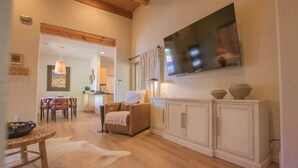Un salón amplio con piso de madera, un sofá, una mesa de comedor y un televisor montado en la pared.