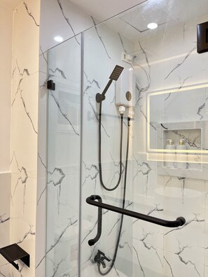 Une salle de bain moderne dotée d’une douche à parois de verre, de murs en marbre et d’une main courante noire.