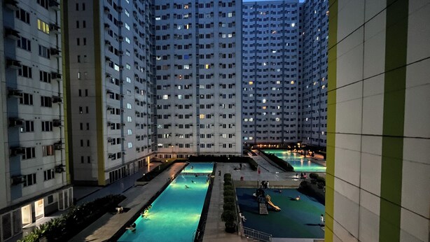 Un edificio residencial de gran altura con varios balcones y un patio central con piscinas.