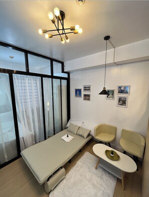Une chambre moderne équipée d’un lit, de deux chaises, d’une petite table et d’un luminaire fixé au plafond.