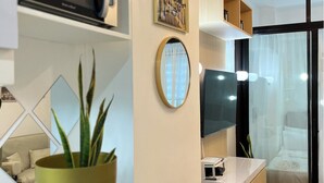 Una habitación de hotel moderna con televisión de pantalla plana, una mesita de noche, una cama con dosel y un ventanal con cortinas translúcidas.