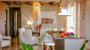 Un espace de repas moderne avec un îlot central, des chaises blanches et un plafond en bois.
