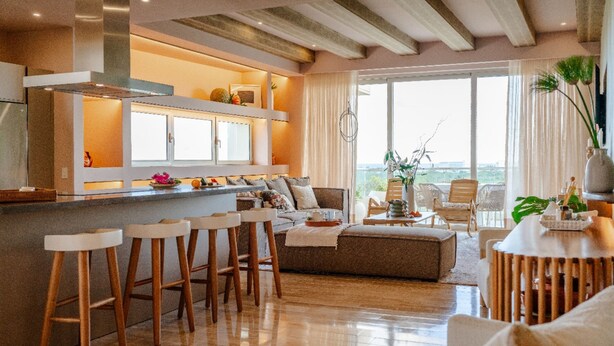 Une cuisine moderne avec un coin bar, un espace salon comprenant un canapé et des fauteuils, et une vue sur l’extérieur.