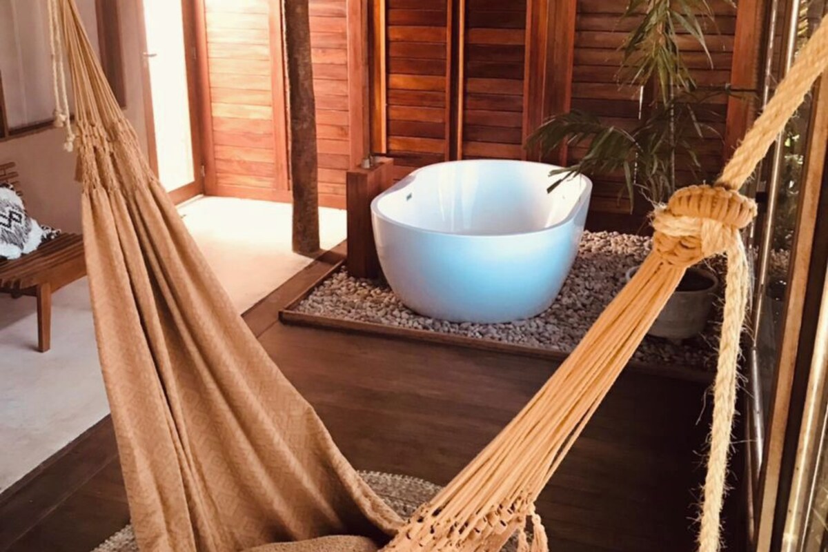 A hammock chair in a wooden room with a large white basin on a woven mat.