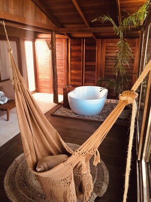 A hammock chair in a wooden room with a large white basin on a woven mat. - Aloha Village Hotel (Amontada)