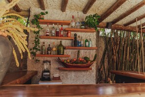 A rustic bar area with wooden shelves holding various bottles and a fruit bowl. - Aloha Village Hotel (Amontada)