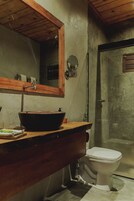 Uma casa de banho com toucador de madeira, um espelho grande, lavatório preto embutido e sanita branca.
