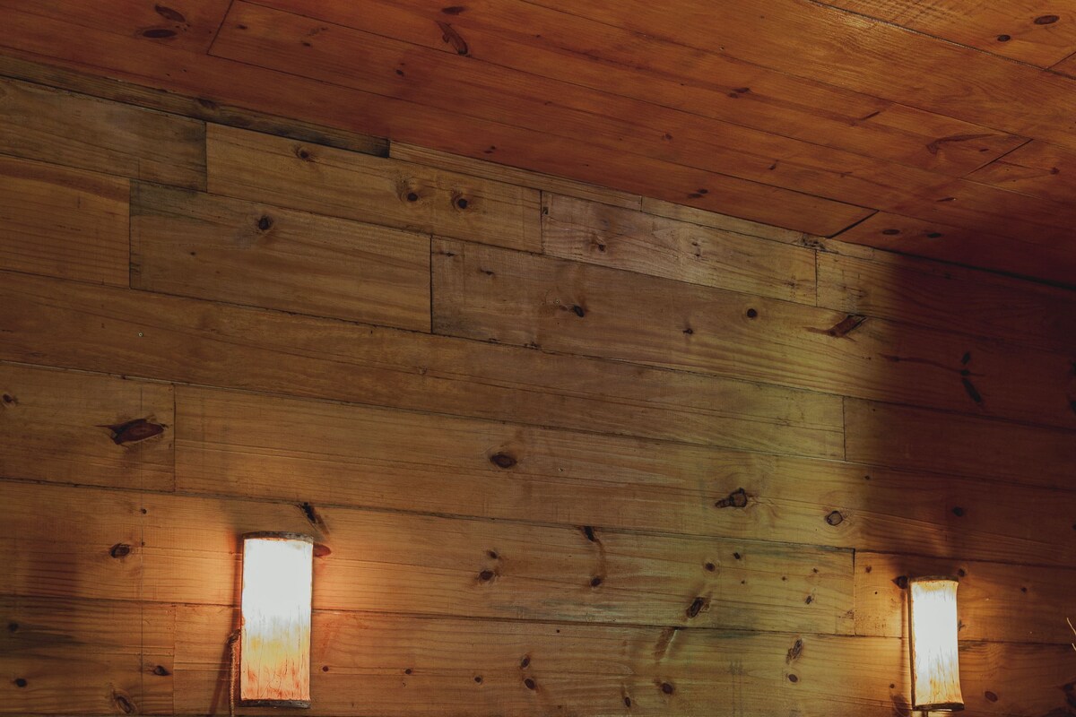 A wooden cabin room with two beds, each with white linens and pillows. There are wall-mounted lamps on either side of the beds.