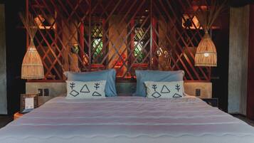 Una cama grande con un edredón blanco y rosa a rayas, dos almohadas azules y un cabecero decorativo con diseño de celosía.