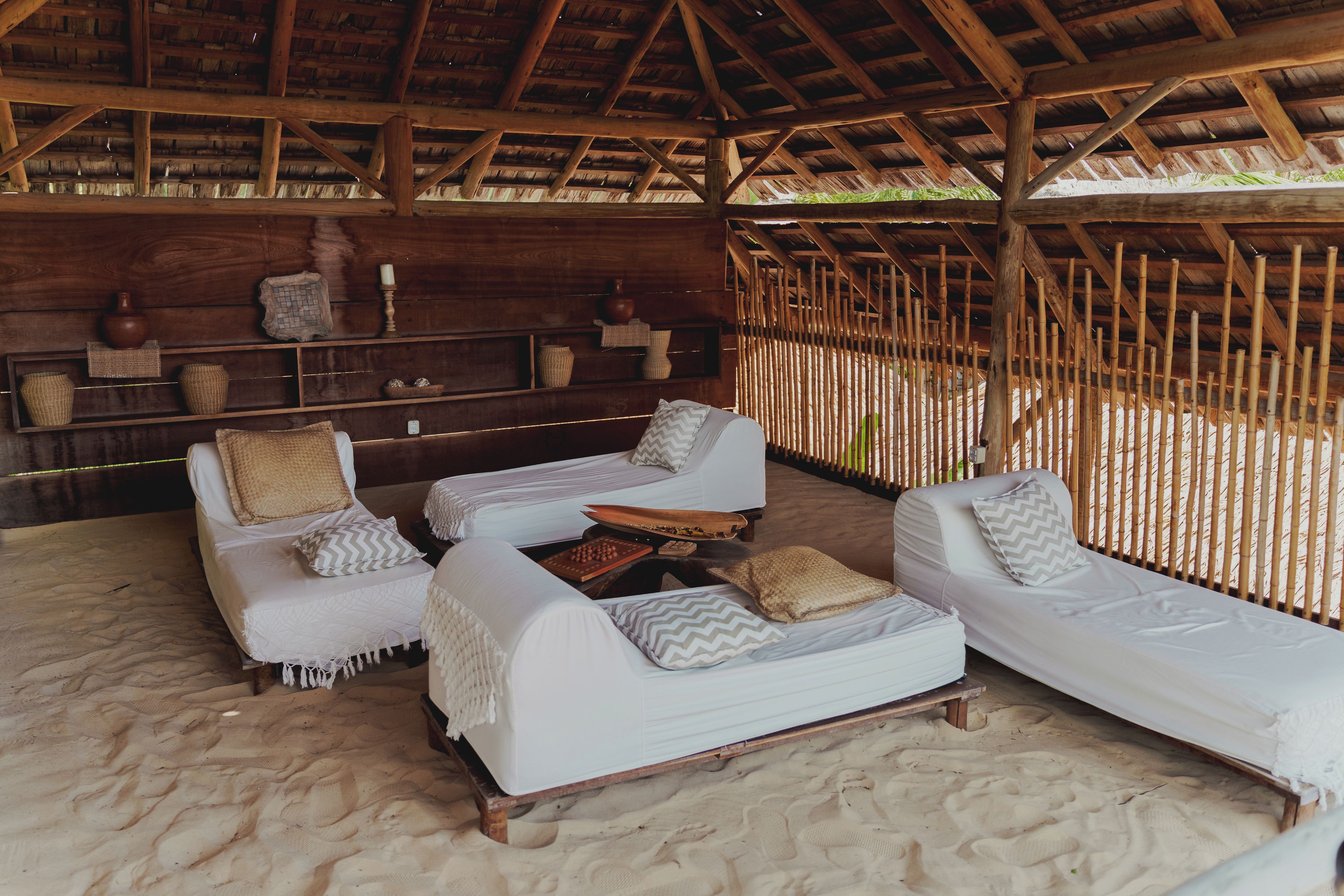 Um espaço de relaxamento à beira-mar com duas cadeiras de praia brancas, uma mesa pequena e uma estante de madeira com objetos decorativos.