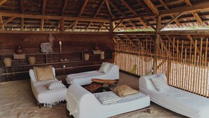A beachside lounge with two white lounge chairs, a small table, and a wooden shelf with decorative items. - Aloha Village Hotel (Amontada)
