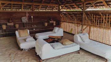 Um espaço de relaxamento à beira-mar com duas cadeiras de praia brancas, uma mesa pequena e uma estante de madeira com objetos decorativos.