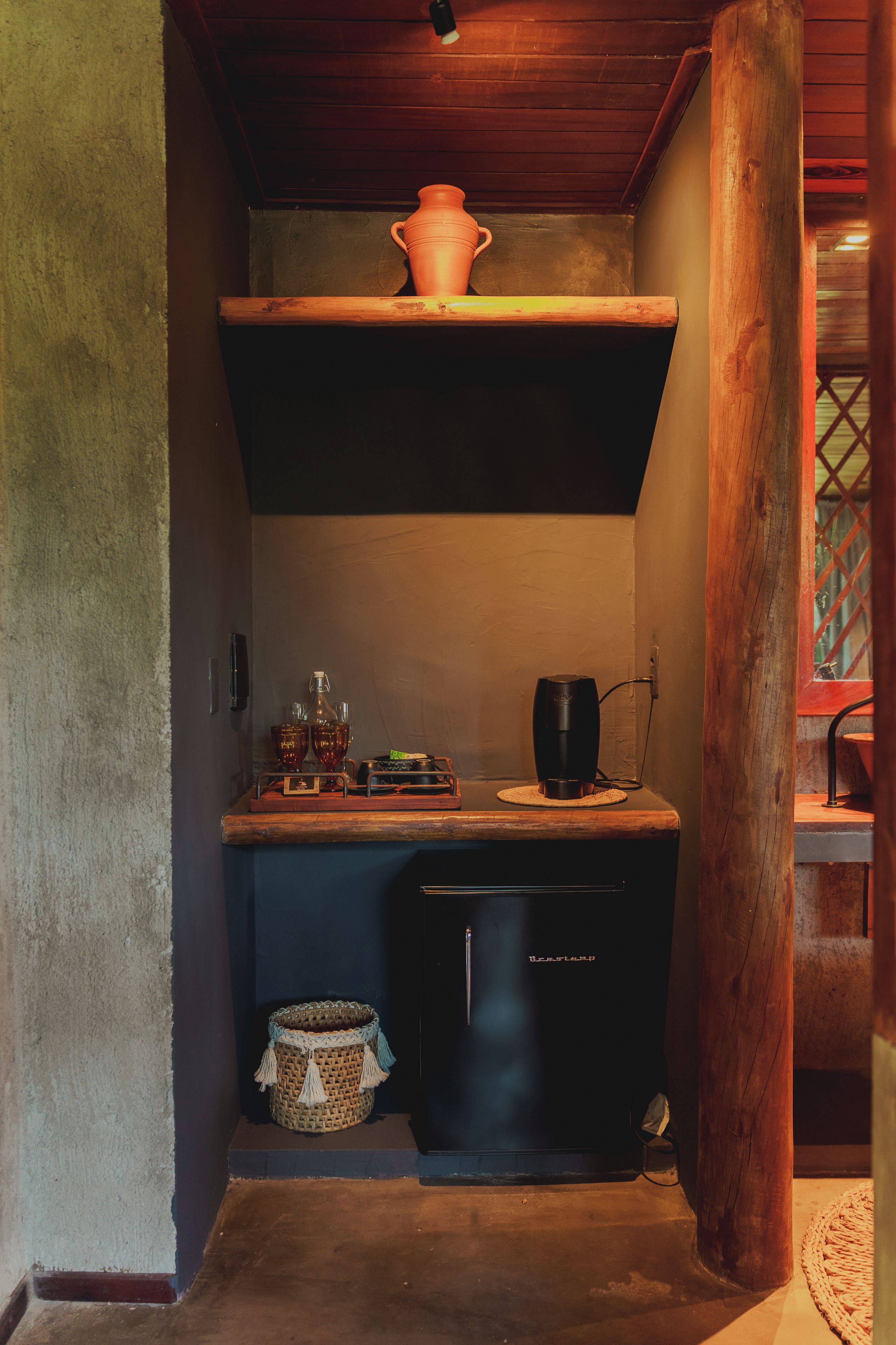 Cocina compacta con refrigerador, cafetera y repisa con una olla.