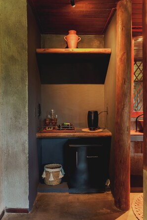 A compact kitchen with a refrigerator, a coffee maker, and a shelf with a pot. - Aloha Village Hotel (Amontada)