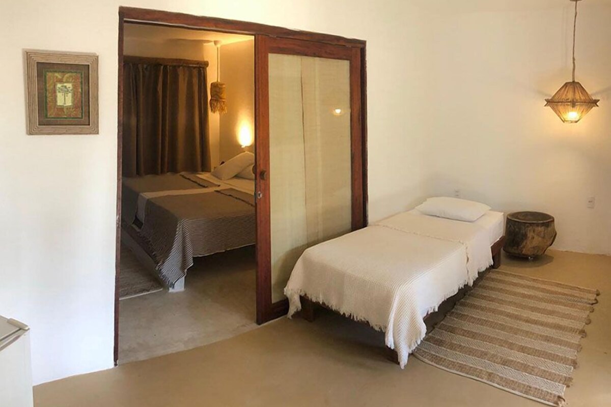 A bedroom with a bed, a bedside table, a lamp, and a door leading to another room.