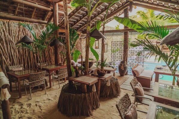 An outdoor seating area with rustic furniture, a pool, and tropical plants. - Aloha Village Hotel (Amontada)