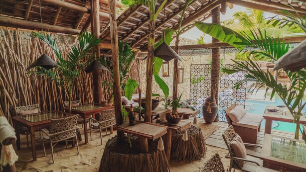 Un área de estar al aire libre con muebles rústicos, una piscina y plantas tropicales.