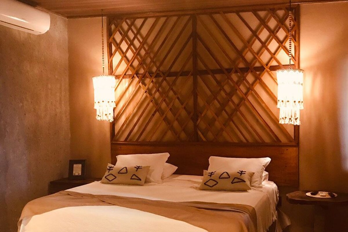 A bedroom with a wooden headboard, a large bed, two bedside tables, and two wall-mounted lamps.