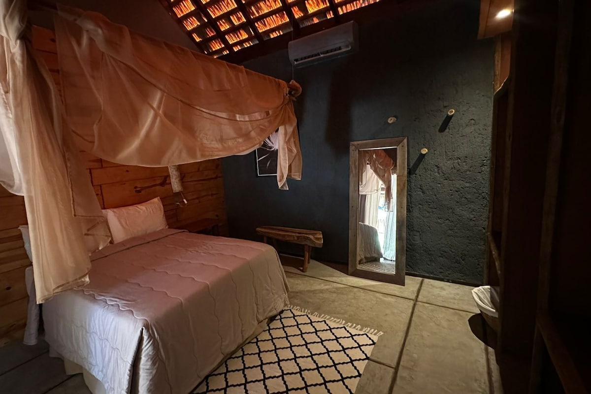 A cozy bedroom with a canopy bed, a wooden headboard, a bench, and a mirror on the wall.