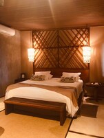 Quarto com cabeceira de madeira, uma cama grande, duas mesas de cabeceira e duas luminárias de parede.