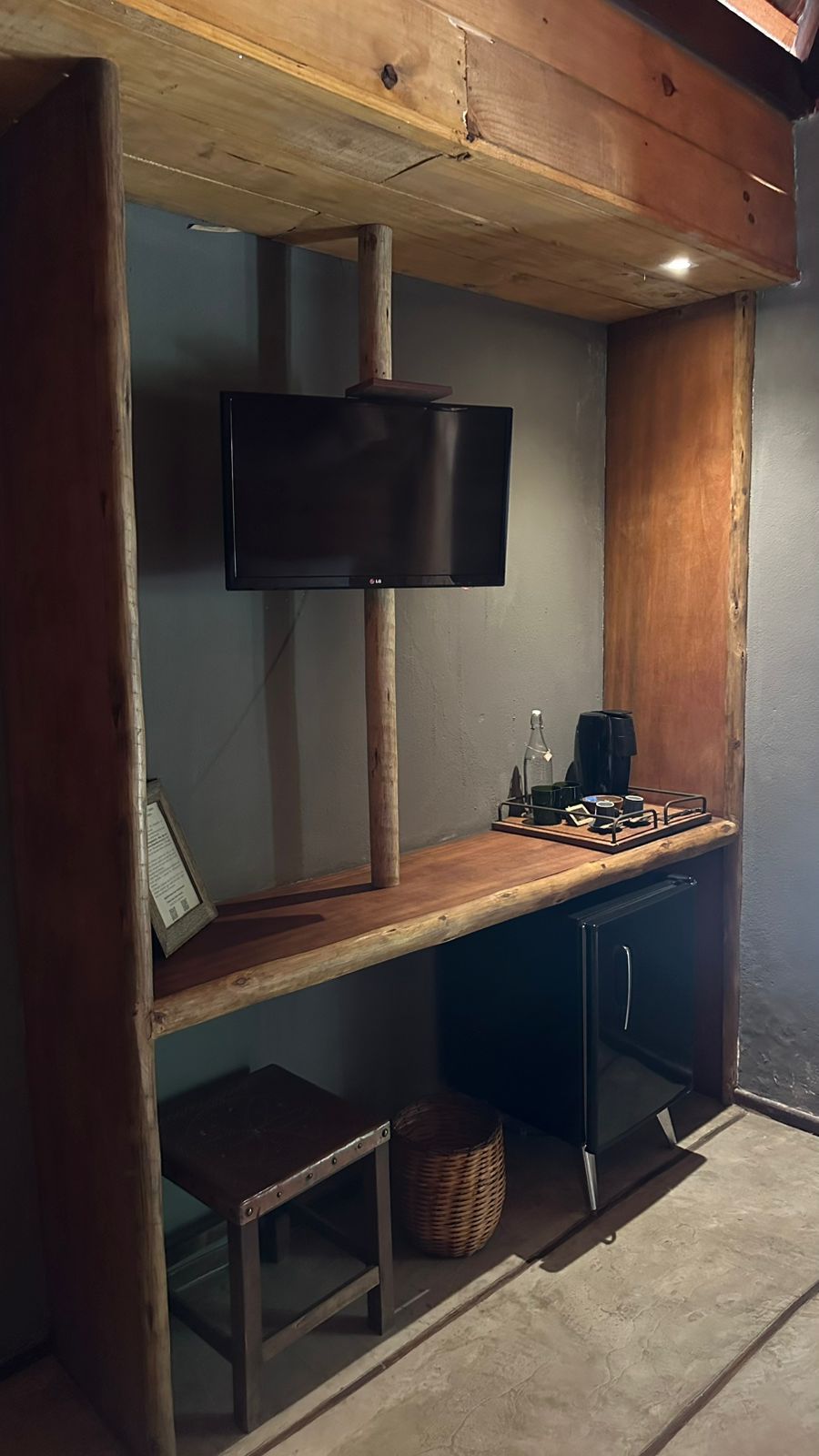 Una stanza con una scrivania in legno, una televisione a muro, uno sgabello e un cesto.