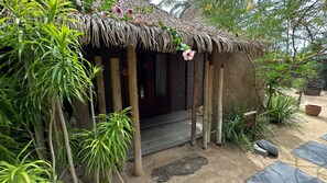 A rustic hut with a thatched roof, surrounded by tropical plants and a wooden deck. - Aloha Village Hotel (Amontada)
