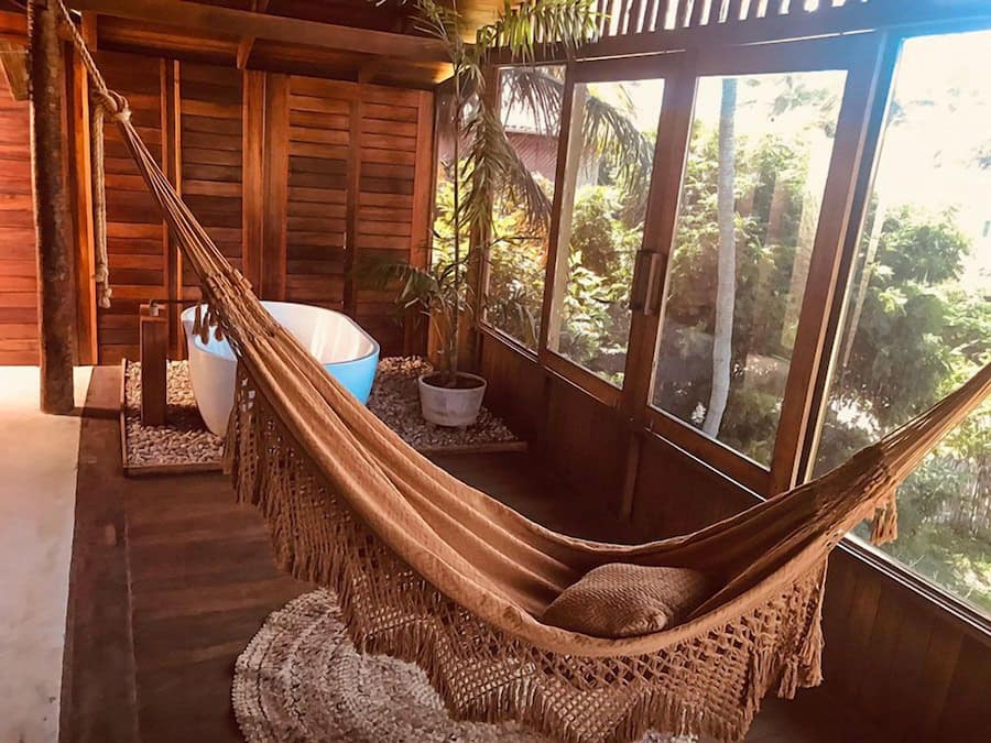A hammock in a wooden cabin with a view of greenery outside.