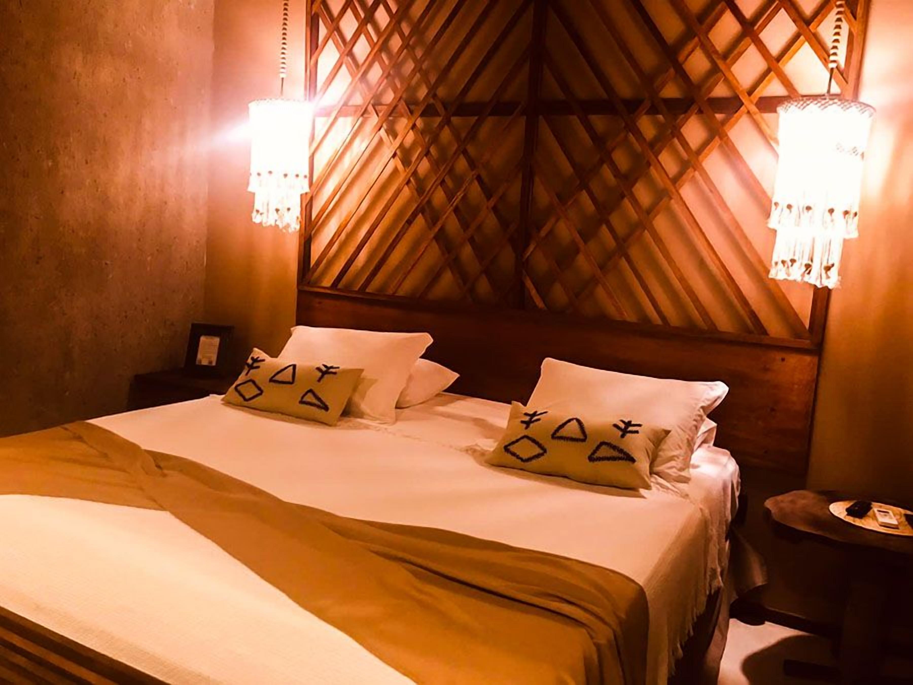 Una cama con cabecera de madera, dos lámparas de noche y almohadones decorativos.